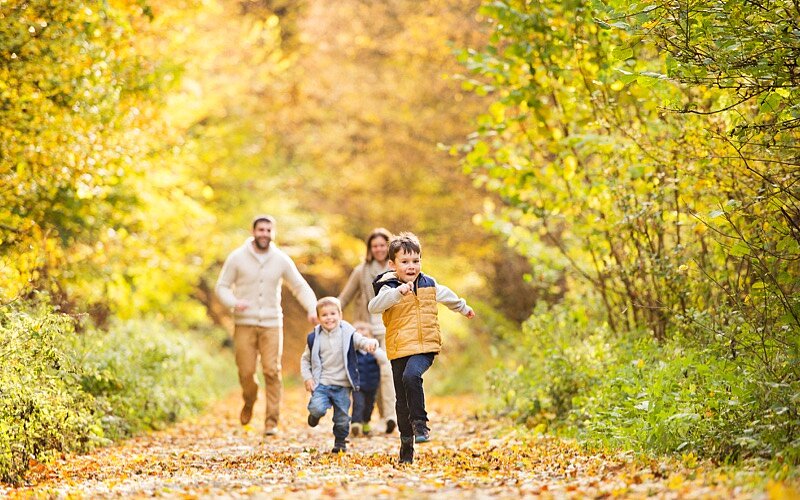 Eine junge Familie mit drei kleinen Kindern läuft fröhlich durch einen herbstlichen Wald.