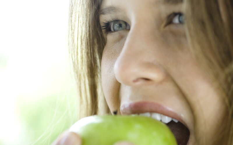 Junges Mädchen beißt in einen grünen Apfel