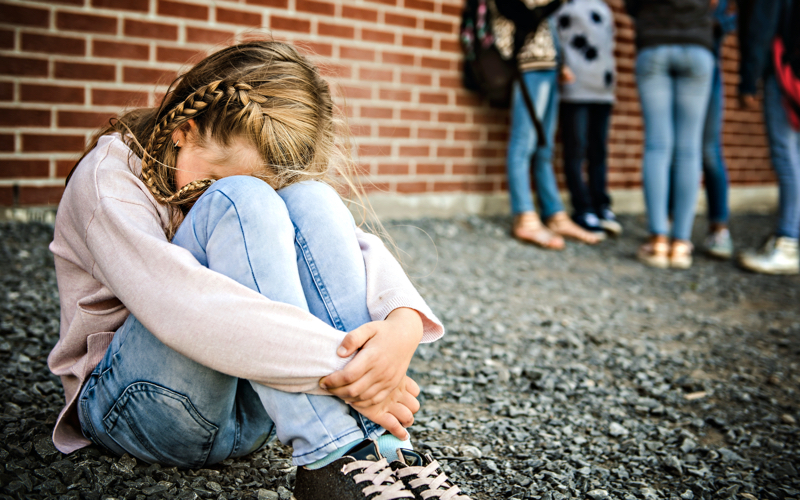 Ein junges Mädchen sitzt allein auf dem Pausenhof und vergräbt ihren Kopf zwischen den Knien.