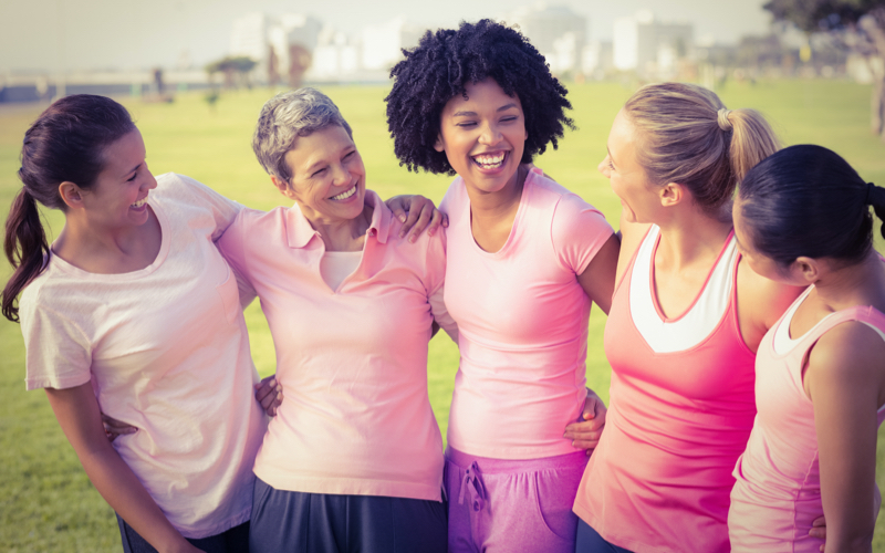 Eine Gruppe junger, sportlicher Frauen steht lächelnd im sommerlichen Park zusammen.