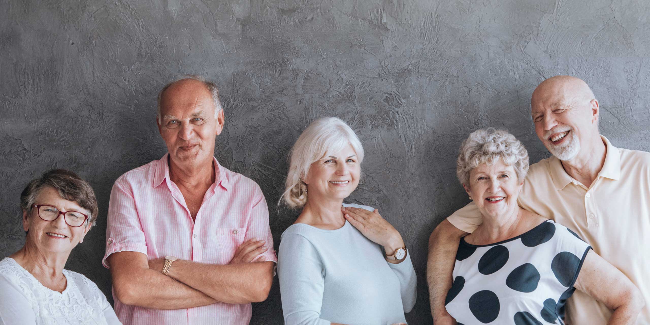 Eine Gruppe älterer lachender Menschen vor einer grau schattierten Wand